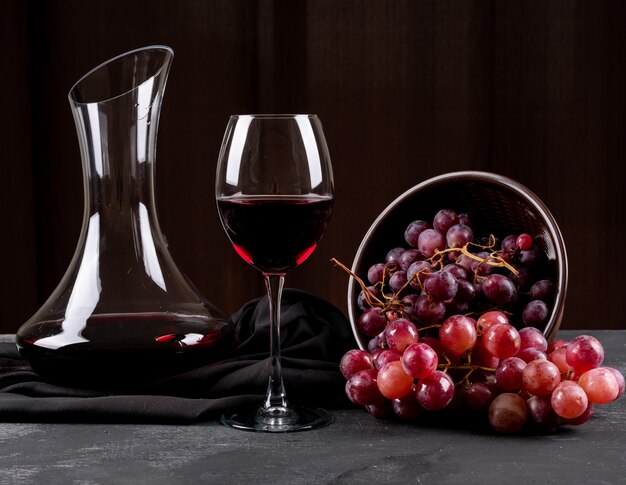 Vista lateral do jarro com vinho tinto e uva no escuro horizontal