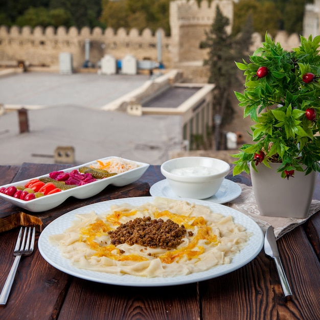 Vista lateral do macarrão caucasiano guru khingal do azerbaijão com carne picada frita e cebola com molho de creme de leite e picles com vista da cidade