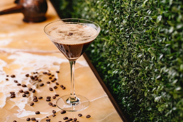 Vista lateral do martini de chocolate com canela de especiarias em vidro e grãos de café na mesa