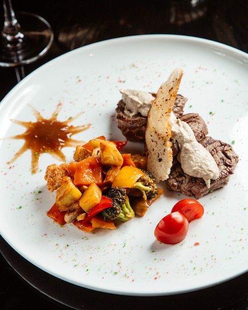 Vista lateral do medalhão de carne grelhada com molho e legumes em um prato branco em cima da mesa