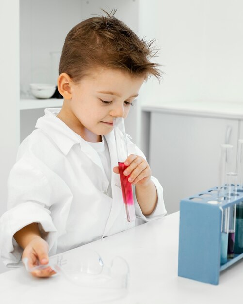 Vista lateral do menino cientista no laboratório com tubos de ensaio fazendo experiências