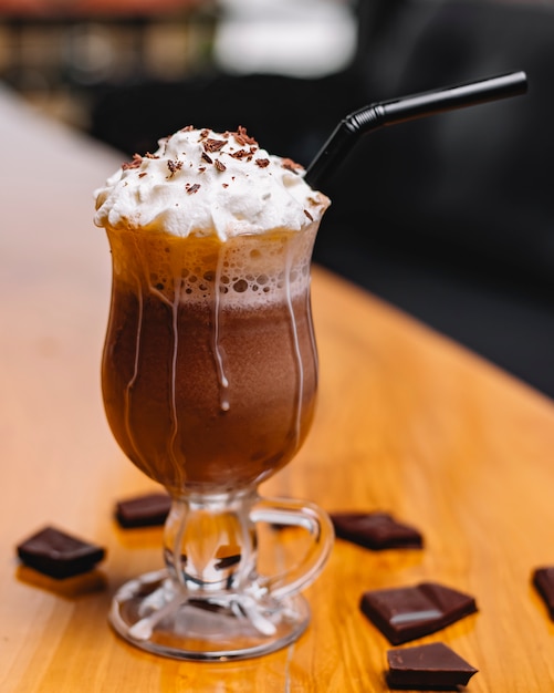 Vista lateral do milkshake de chocolate com chantilly em um copo em uma mesa de madeira