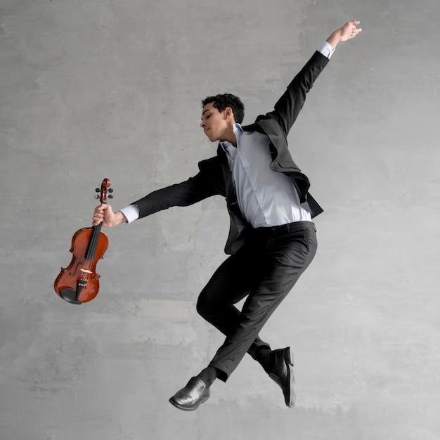 Vista lateral do músico masculino segurando o violino e posando no ar