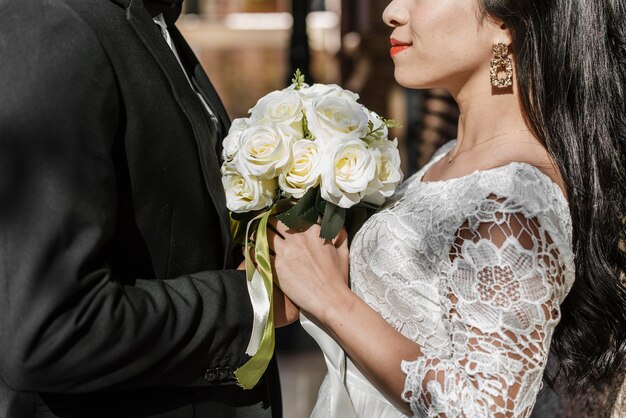 Vista lateral do noivo e da noiva segurando um buquê de flores