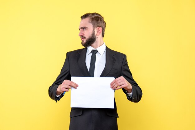 Vista lateral do perfil do jovem empresário segurando um papel em branco na parede amarela