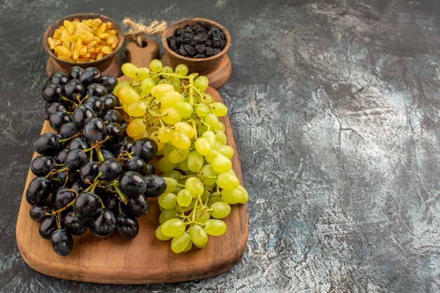 Vista lateral em close-up de frutas, cachos de uvas verdes e pretas no tabuleiro de tigelas de frutas secas
