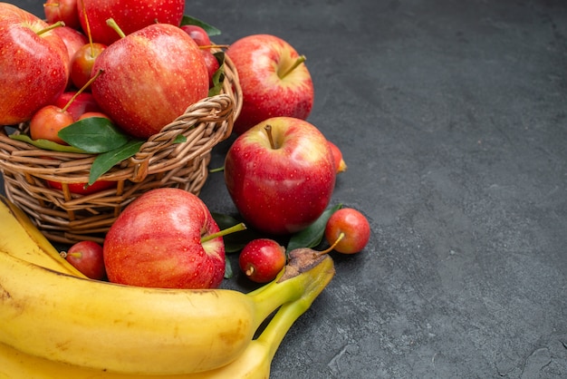 Vista lateral em close-up de frutas, cesta de madeira com maçãs e cerejas, bananas