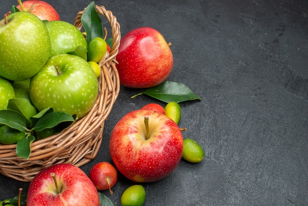 Vista lateral em close-up de uma cesta de frutas de madeira com maçãs verdes com folhas ao lado das bagas e frutas