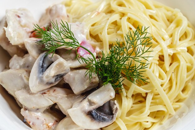 Vista lateral fettuccini Alfredo com molho de cogumelos grelhados e endro em um prato