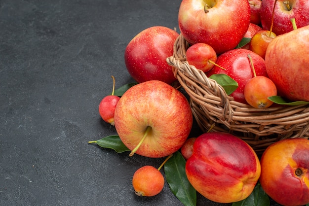 Vista lateral frutas a cesta de madeira com maçãs cerejas nectarina com folhas