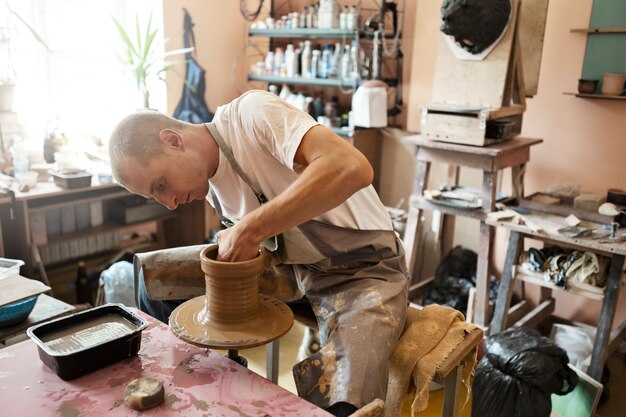Vista lateral homem argila esculpindo dentro de casa