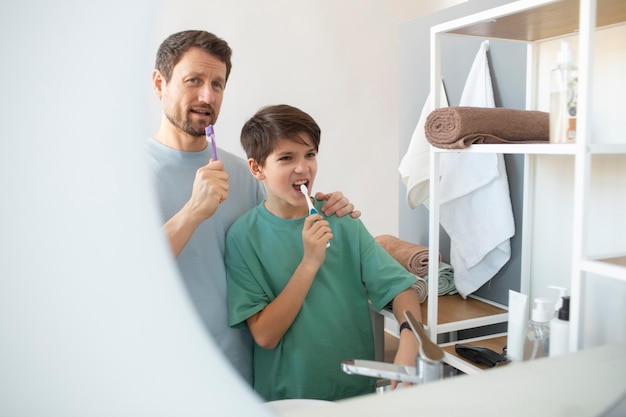 Vista lateral homem e menino escovando os dentes