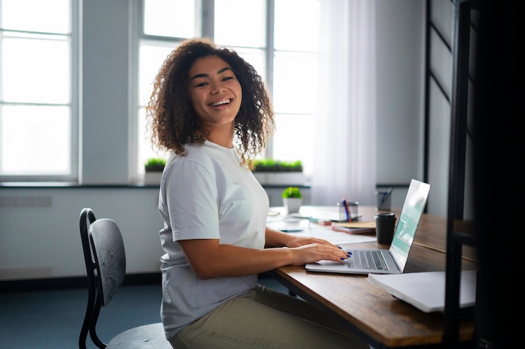 Os incentivos para empresas ajudam também os mais jovens. Na imagem, uma adolescente está em seu primeiro emprego. Ela está sorrindo, sentada em sua mesa, com um notebook e alguns papéis. | Fonte: Freepik