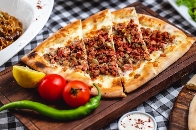 Vista lateral pide pão com carne moída tomate hor pimenta verde queijo e fatia de limão em uma placa