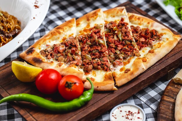 Vista lateral pide pão com carne moída tomate hor pimenta verde queijo e fatia de limão em uma placa