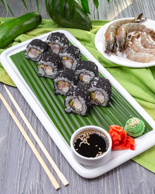 Vista lateral preto califórnia roll tobiko caviar abacate creme de queijo camarão wasabi gengibre e molho de soja em um prato