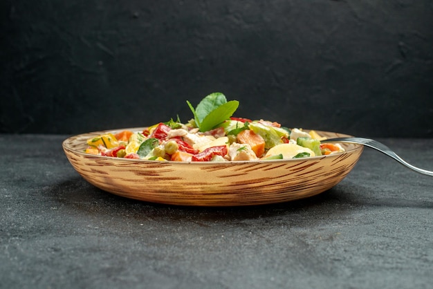 Vista lateral próxima de uma tigela de salada de legumes com garfo ao lado em uma mesa cinza escura em fundo cinza escuro