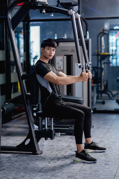 Vista lateral, retrato jovem bonito em roupas esportivas, sentado para fazer exercícios de pressão no peito da máquina no ginásio moderno.