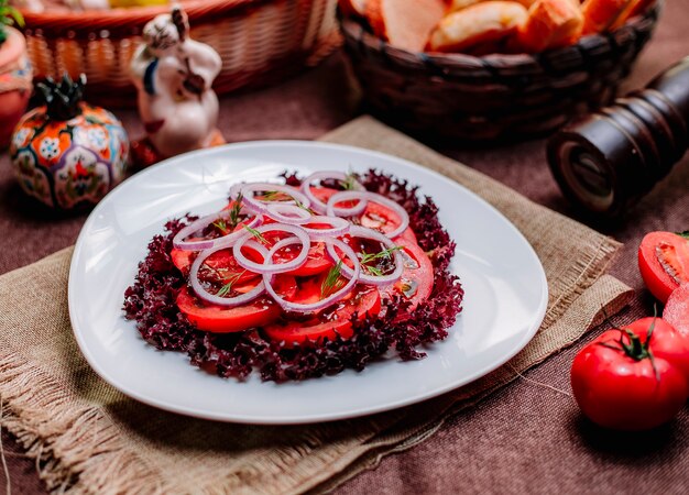 Vista lateral salada de tomate fatiado de tomate com cebola roxa e alface em um prato