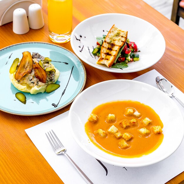 Vista lateral sopa de lentilha com biscoitos e com purê de batatas salada de legumes e suco em cima da mesa