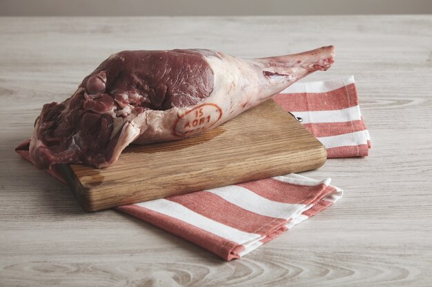 Vista lateral superior na perna de cordeiro crua islandesa, isolada em uma toalha listrada e na placa de madeira.