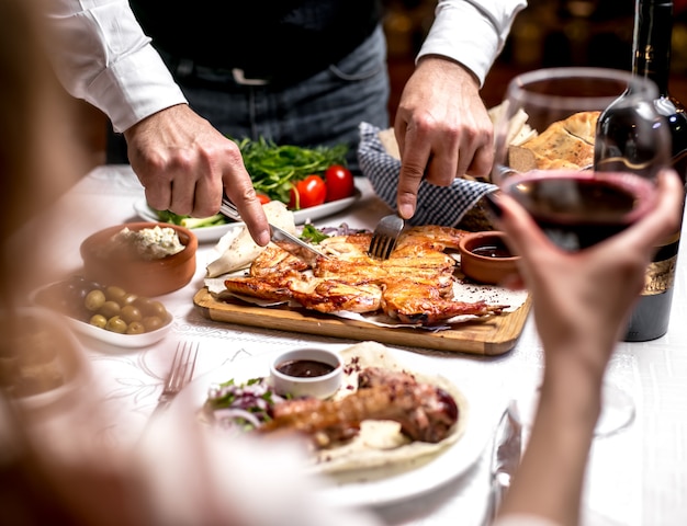 Vista lateral, um homem corta tabaco no pão pita com molho e cebola com verduras e tomates