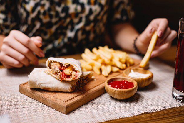 Vista lateral, uma mulher come frango doner no pão pita com batatas fritas com ketchup e maionese