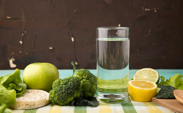 Foto grátis vista lateral verde frutas e legumes maçã brocoli alface estaladiço crocante copo de água fatia de limão e limão