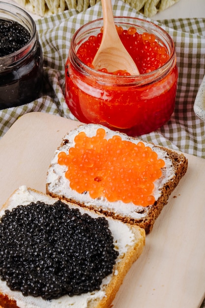 Vista lateral vermelho e preto caviar torrada de centeio e pão branco com queijo cottage caviar vermelho e caviar preto em uma placa