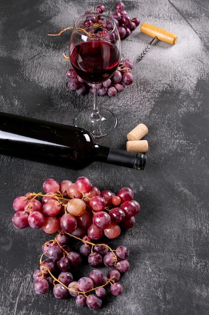 Vista lateral vinho tinto com uva na pedra preta vertical