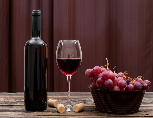 Vista lateral vinho tinto em garrafa, copo e uva na mesa escura e horizontal