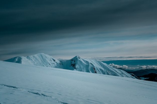 Vista panorâmica de montanhas cobertas de neve tocando as nuvens