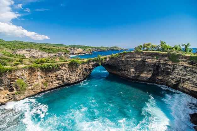 Vista panorâmica de praia quebrada em Nusa Penida, Bali, Indonésia. Céu azul, água turquesa.