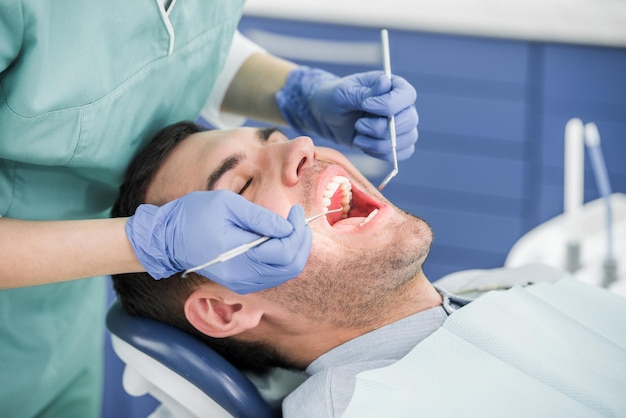 Vista recortada do dentista com luvas de látex examinando o paciente com a boca aberta
