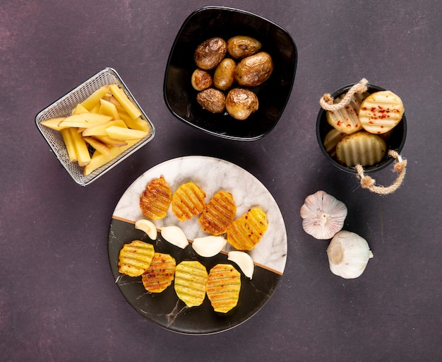 Vista superior batatas grelhadas e batatas picadas com flocos de pimenta seca e alho em fundo cinza escuro