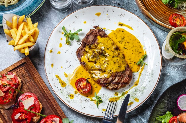 Vista superior bife grelhado de carne vermelha com molho de tomate menta e batatas fritas em cima da mesa