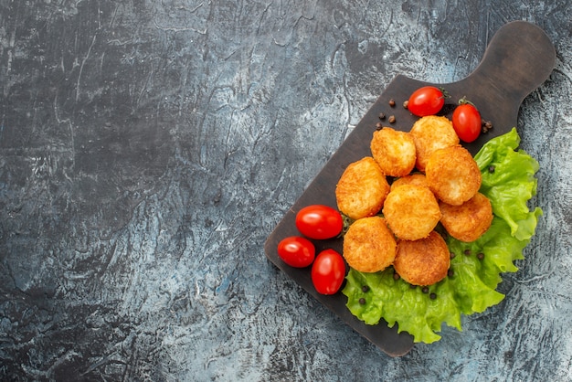 Vista superior bolinhas de queijo frito, tomate cereja, alface em uma tábua na mesa