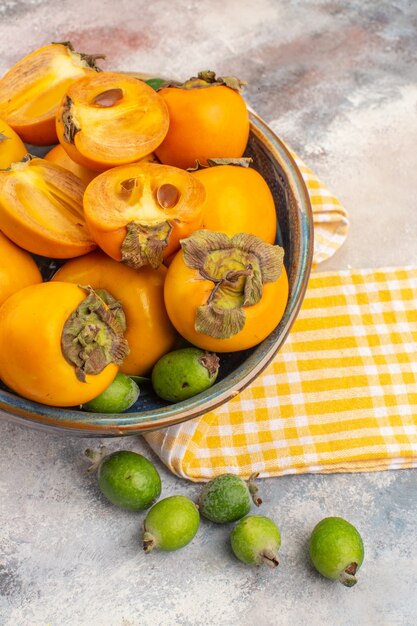 Foto grátis vista superior caqui fresco em uma tigela toalha de cozinha amarela feykhoas em fundo nu