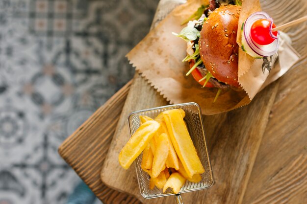 Vista superior close-up de hambúrguer e batatas fritas na placa de madeira