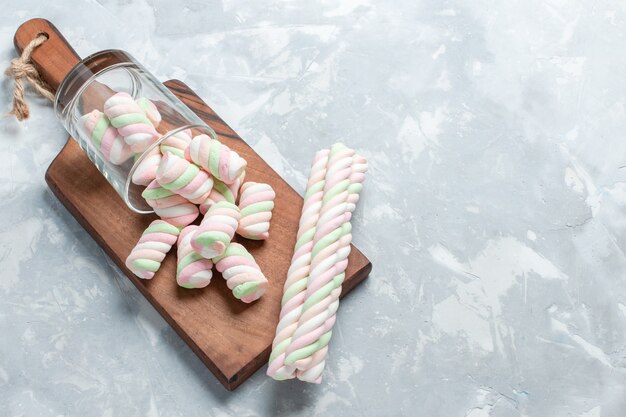 Vista superior colorida deliciosos marshmallows pouco formados docinhos no chão branco claro.