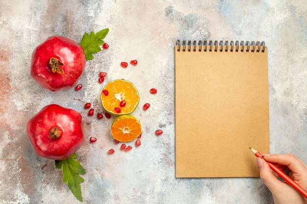 Vista superior com romãs vermelhas rodelas de limão lápis vermelho no caderno de mão de uma mulher