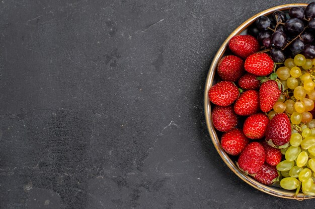 Vista superior composição de frutas morangos uvas framboesas e tangerinas dentro da bandeja na mesa escura