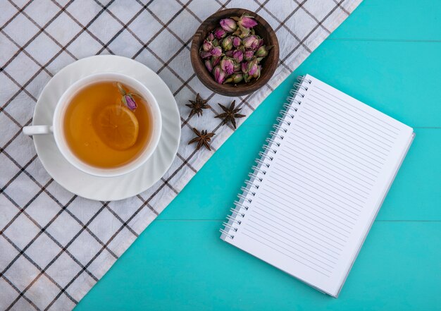 Vista superior cópia espaço xícara de chá com uma fatia de limão e um notebook com flores secas sobre um fundo azul claro