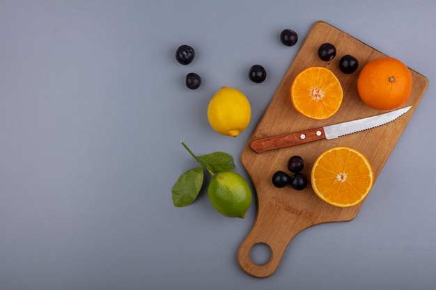 Vista superior copie fatias de laranja em uma tábua com faca e ameixa cereja limão e lima em fundo cinza
