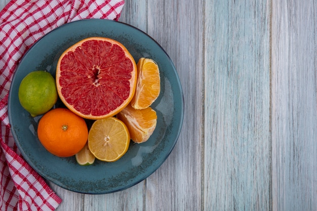 Vista superior copie metades de toranja com laranja e limão com limão em um prato sobre uma toalha quadriculada em um fundo cinza