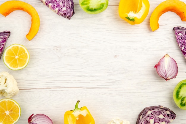 Vista superior corte de vegetais repolho roxo tomate verde abóbora cebola vermelha pimentão amarelo couve-flor limão na superfície de madeira branca com espaço livre