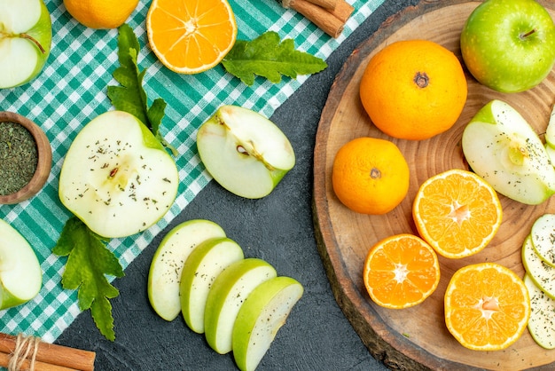 Vista superior, corte maçãs e tangerinas em palitos de canela em tábua redonda rústica sobre toalha de mesa verde