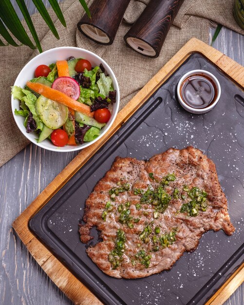 Vista superior costeleta grelhada de carne com salada de legumes e molho no quadro-negro