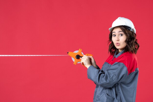 Vista superior da arquiteta imaginando mulher de uniforme com capacete abrindo a fita métrica em fundo vermelho isolado