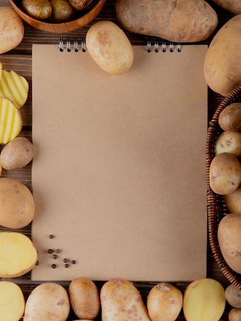 Vista superior da batata inteira e cortada com pimenta preta e bloco de notas com espaço de cópia